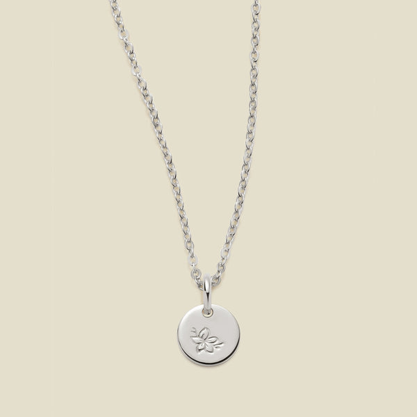 A silver chain necklace with a round silver disc pendant featuring an engraved cherry blossom flower design, displayed against a solid light beige background.