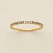 A gold ring featuring a single row of small round-cut light blue-grey gemstones, photographed on a clean, solid, warm off-white background.