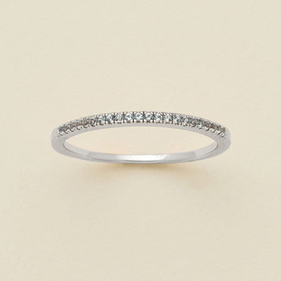 A silver ring featuring a single row of small round-cut light blue-grey gemstones, photographed on a clean, solid, warm off-white background.