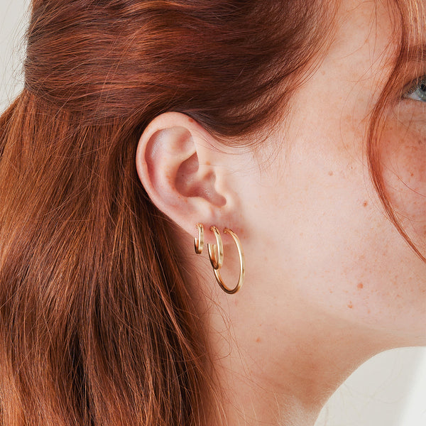A close-up of a person's ear wearing three different sizes of the same polished gold hoop earrings.