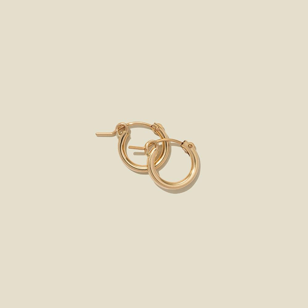 A pair of gold hoop earrings with a polished finish, displayed against a solid light beige background.
