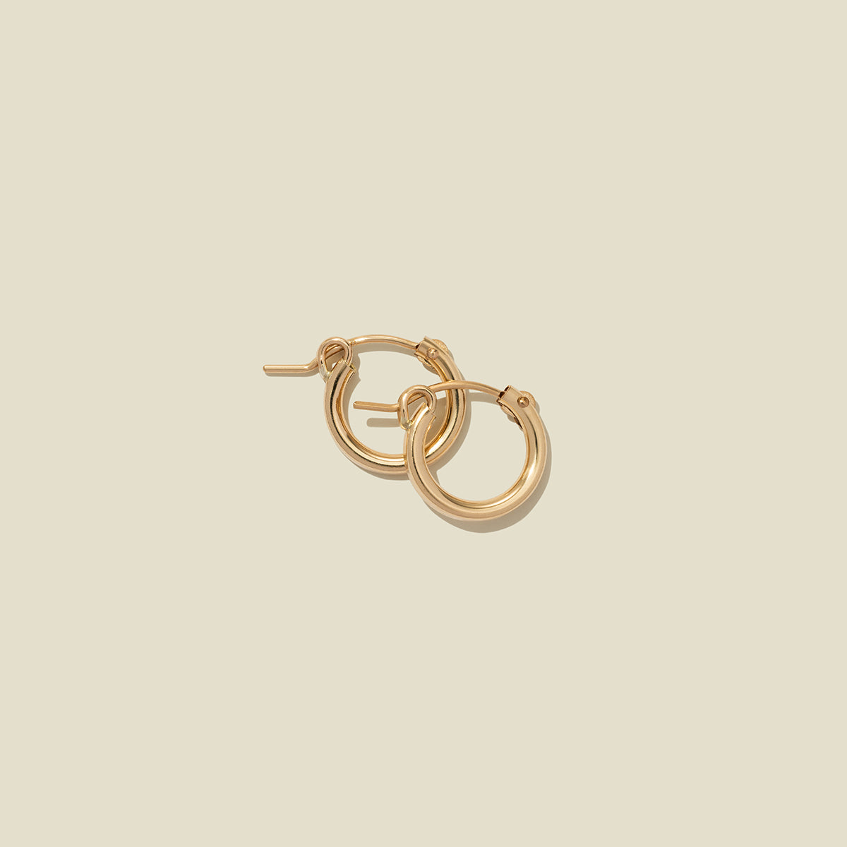 A pair of gold hoop earrings with a polished finish, displayed against a solid light beige background.
