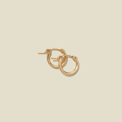 A pair of gold hoop earrings with a polished finish, displayed against a solid light beige background.