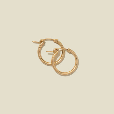 A pair of gold hoop earrings with a polished finish, displayed against a solid light beige background.