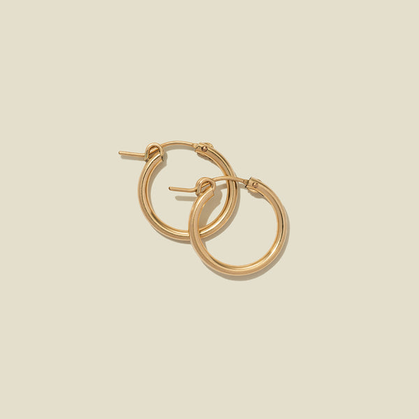 A pair of gold hoop earrings with a polished finish, displayed against a solid light beige background.