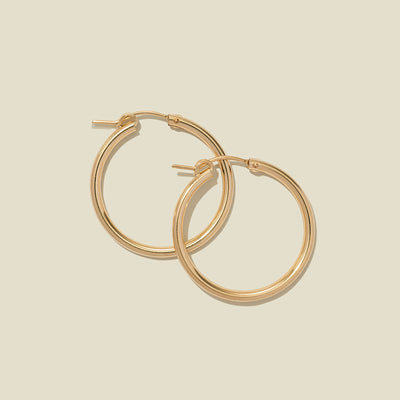 A pair of gold hoop earrings with a polished finish, displayed against a solid light beige background.