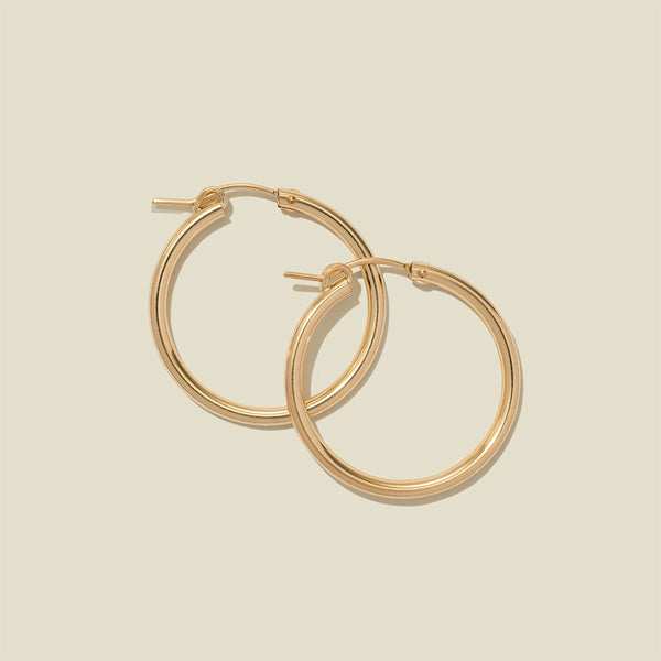 A pair of gold hoop earrings with a polished finish, displayed against a solid light beige background.