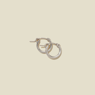 A pair of silver hoop earrings with a polished finish, displayed against a solid light beige background.
