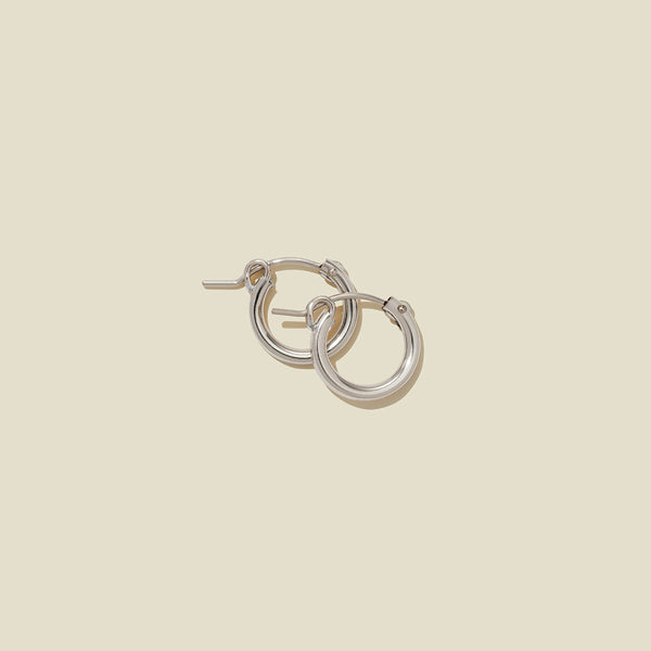 A pair of silver hoop earrings with a polished finish, displayed against a solid light beige background.