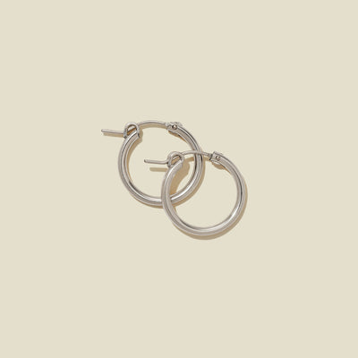 A pair of silver hoop earrings with a polished finish, displayed against a solid light beige background.
