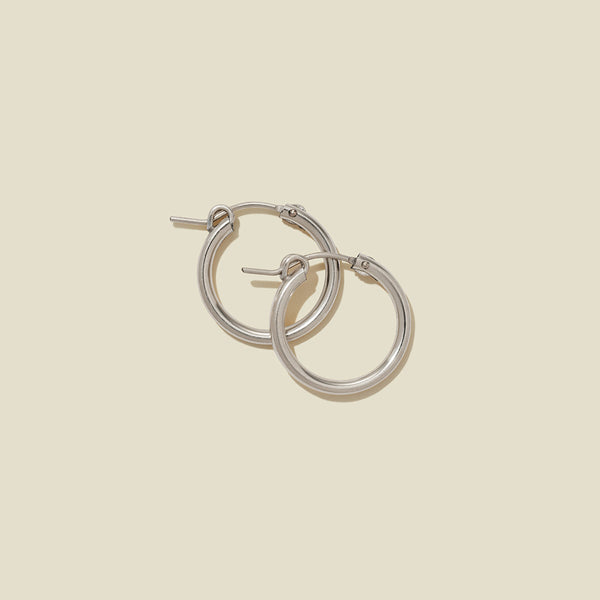 A pair of silver hoop earrings with a polished finish, displayed against a solid light beige background.