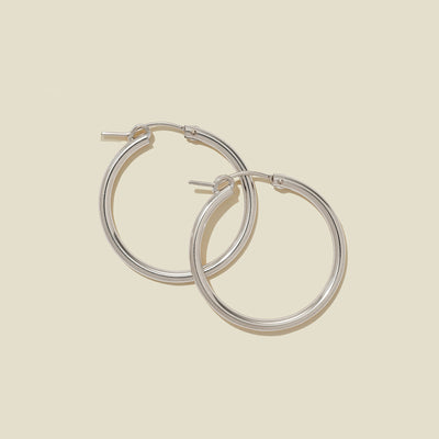 A pair of silver hoop earrings with a polished finish, displayed against a solid light beige background.