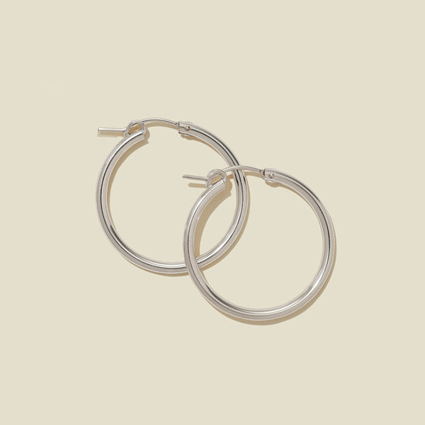 A pair of silver hoop earrings with a polished finish, displayed against a solid light beige background.
