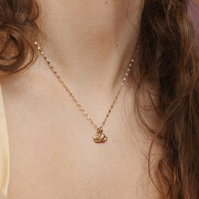 A woman wearing a delicate textured gold chain necklace with two small flower charms.