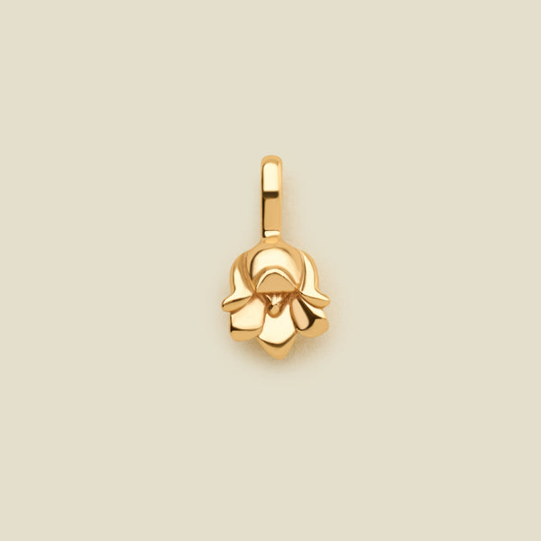 A polished gold lily of the valley flower charm, shown on a solid light beige background.