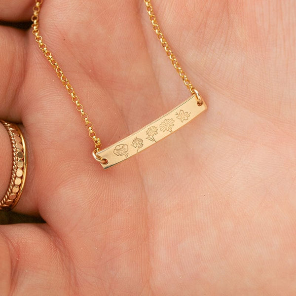 A close-up of a person's hand wearing a delicate gold chain bracelet with a central bar engraved with different flower designs.