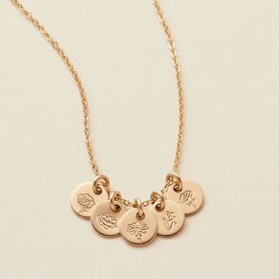 A gif of a delicate gold chain necklace with five small round flat discs, each with their own floral design engraved. The floral designs on different discs change every few seconds.