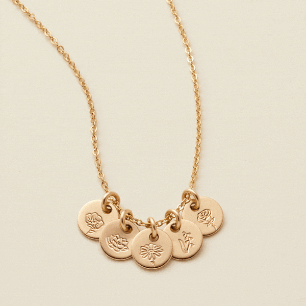A gif of a delicate gold chain necklace with five small round flat discs, each with their own floral design engraved. The floral designs on different discs change every few seconds.