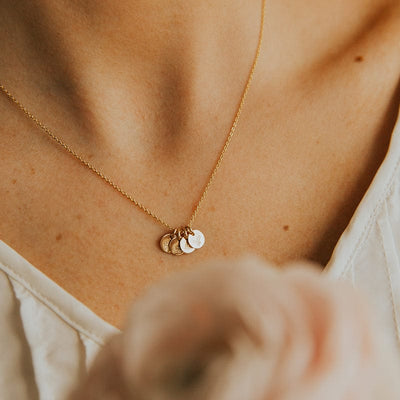 A close-up of a woman wearing a delicate gold chain necklace with four small round flat discs, each with it's own engraved floral design.