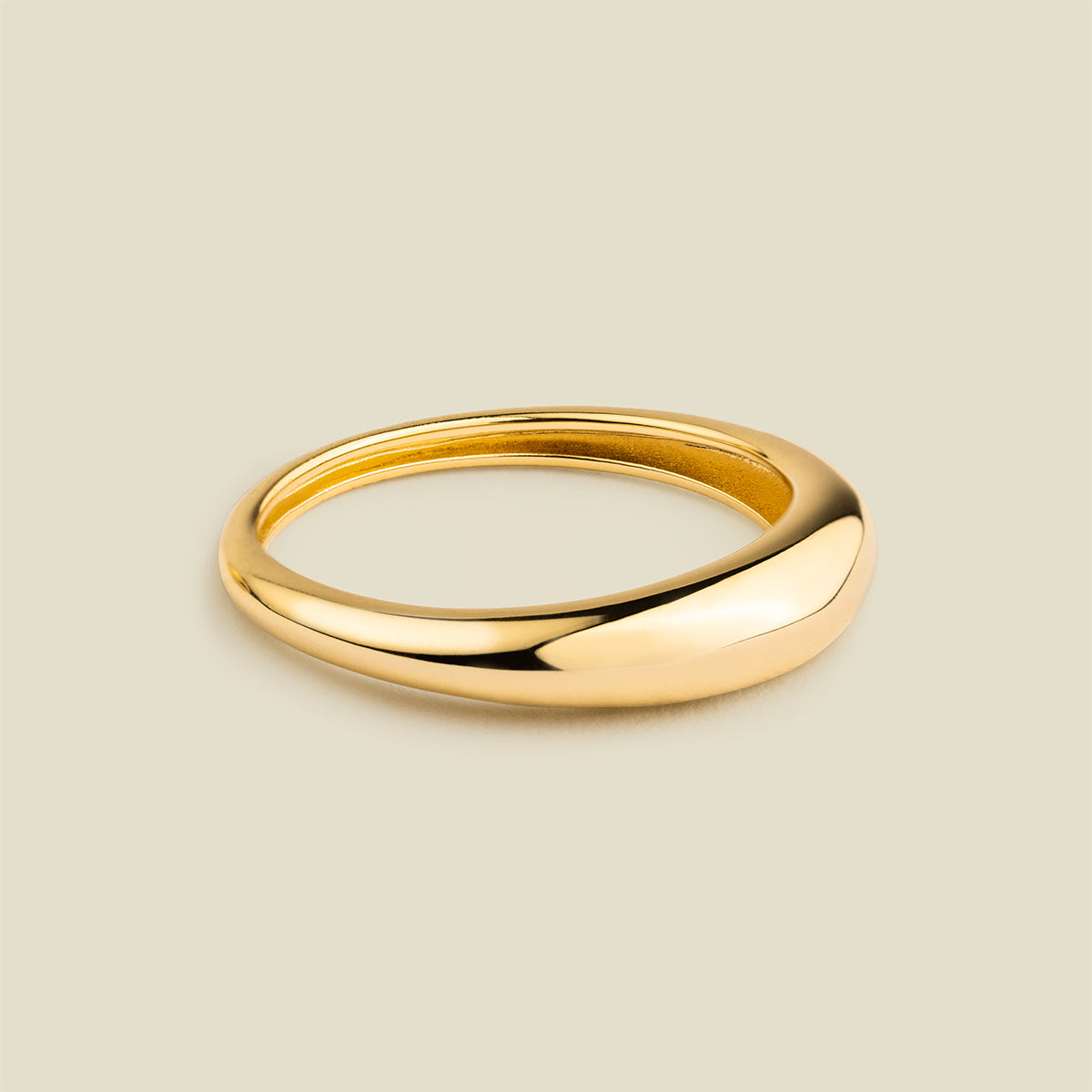 A polished gold band ring with a smooth, rounded organic shape, displayed on a solid light beige background.