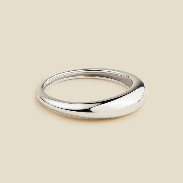 A polished silver band ring with a smooth, rounded organic shape, displayed on a solid light beige background.
