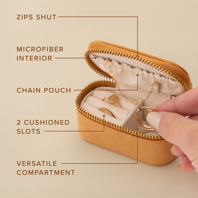 A small tan leather zippered jewelry case shown open with a hand reaching in to grab jewelry out. Over the image are multiple tag lines with lines pointing out features of the case, including 'ZIPS SHUT', 'MICROFIBER INTERIOR', 'CHAIN POUCH', '2 CUSHIONED SLOTS', and 'VERSATILE COMPARTMENT'.