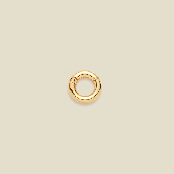 A polished gold ring necklace attachment, shown on a solid light beige background.