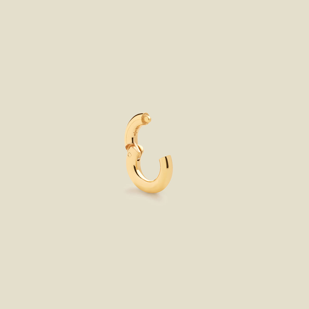 A polished gold ring necklace attachment with an open latch mechanism, shown on a solid light beige background.
