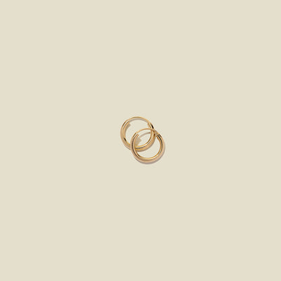 Two small thin gold hoop earrings laying on top of one another, shown on a light beige background.