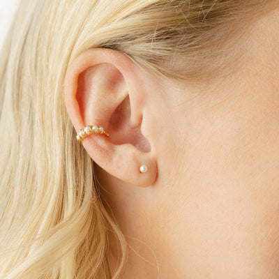 A close-up of a person's ear wearing a small pearl stud and an ear cuff with prong set round pearls.