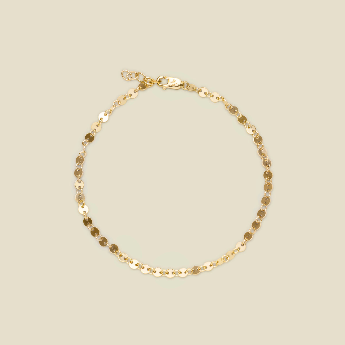 A delicate gold chain bracelet with flat, circular disc links and a lobster clasp, displayed on a solid light beige background.