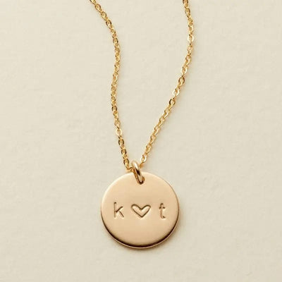 A delicate gold pendant chain necklace with an engraved disc reading 'k ♥ t'.