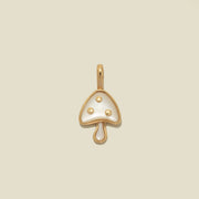 A small mushroom-shaped pendant charm with a gold-tone metal outline and a glossy white stone inlay, featuring three small gold dots on the cap, centered on a light beige background.