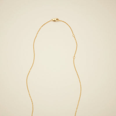 The end of a delicate gold pendant chain, featuring a lobster clasp closure and multiple round rings for attaching the clasp, shown on a solid light beige background.