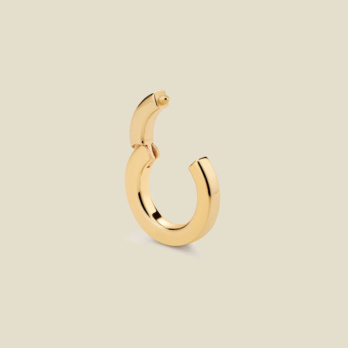 A polished gold round charm attachment for necklaces, with an open center. The hinge clasp at the top is open, and it is set against a solid beige background.