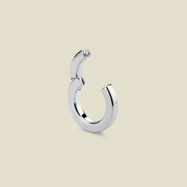 A polished silver round charm attachment for necklaces, with an open center. The hinge clasp at the top is open, and it is set against a solid beige background.