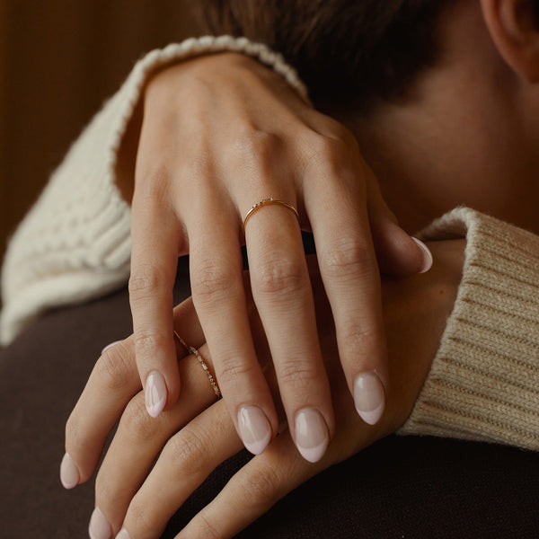 A close-up of a person's hands draped around someone's neck, showcasing multiple gold rings with different patterns and cuts of clear gemstones.