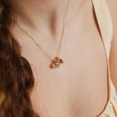A woman wearing a delicate gold chain necklace with four small flower charms.