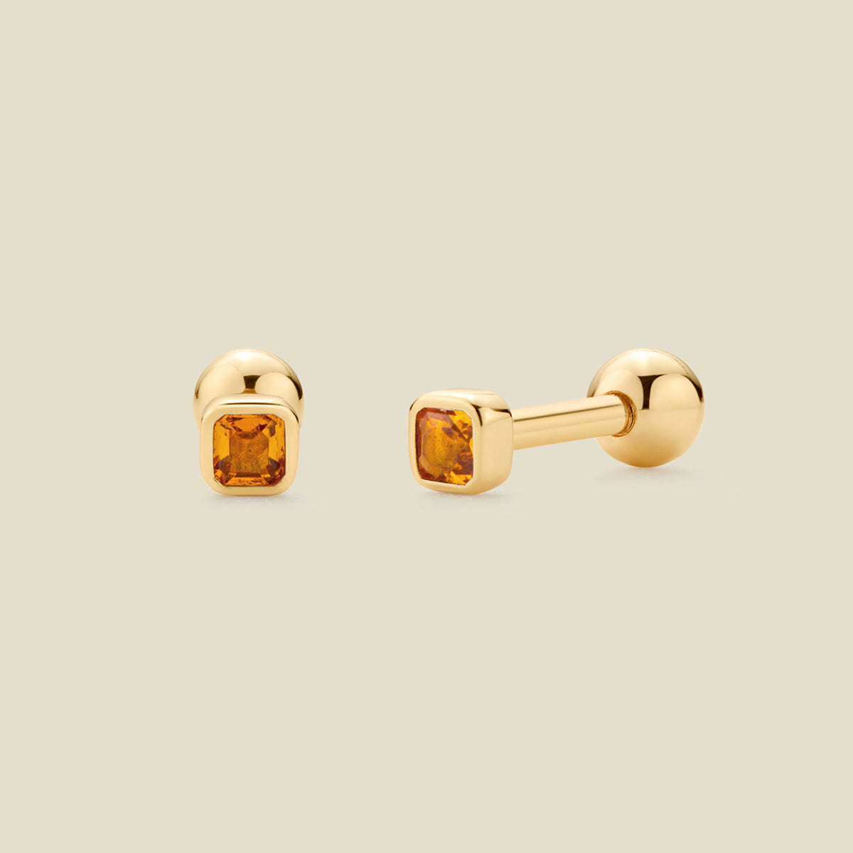 A pair of gold stud earrings with square-cut amber gemstones, shown from both front and side angles on a light beige background.