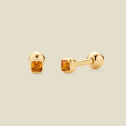 A pair of gold stud earrings with square-cut amber gemstones, shown from both front and side angles on a light beige background.