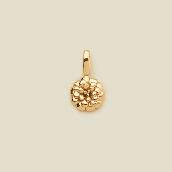 A small polished gold marigold flower charm, shown on a solid light beige surface.