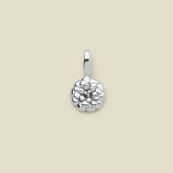 A small polished silver marigold flower charm, shown on a solid light beige surface.