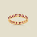 A gold eternity ring featuring a continuous row of square cut pink gemstones, shown on a solid light beige background.