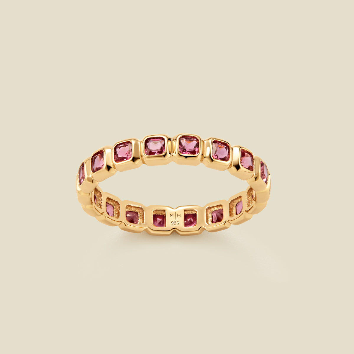 A gold eternity ring featuring a continuous row of square cut pink gemstones, shown on a solid light beige background.