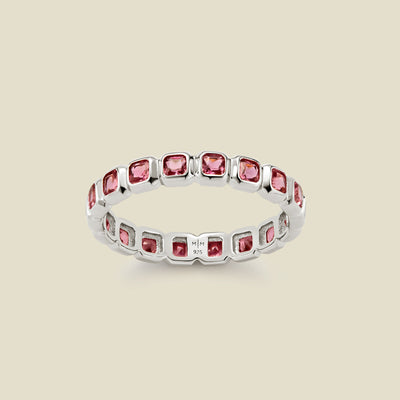 A silver eternity ring featuring a continuous row of square cut pink gemstones, shown on a solid light beige background.