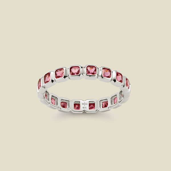 A silver eternity ring featuring a continuous row of square cut pink gemstones, shown on a solid light beige background.
