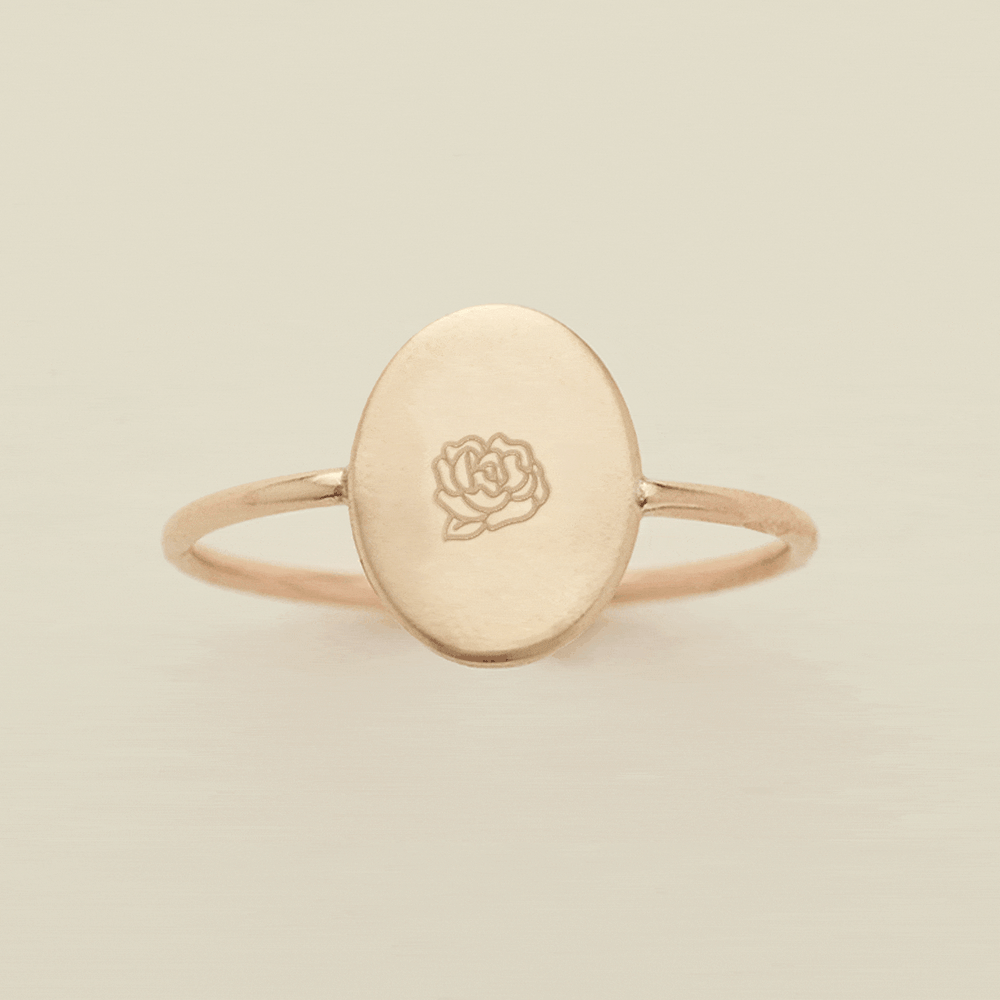 A gif of a dainty gold wire ring with a flat oval in the center, with different engraved designs cycling through one by one. There are initials and various floral motifs.