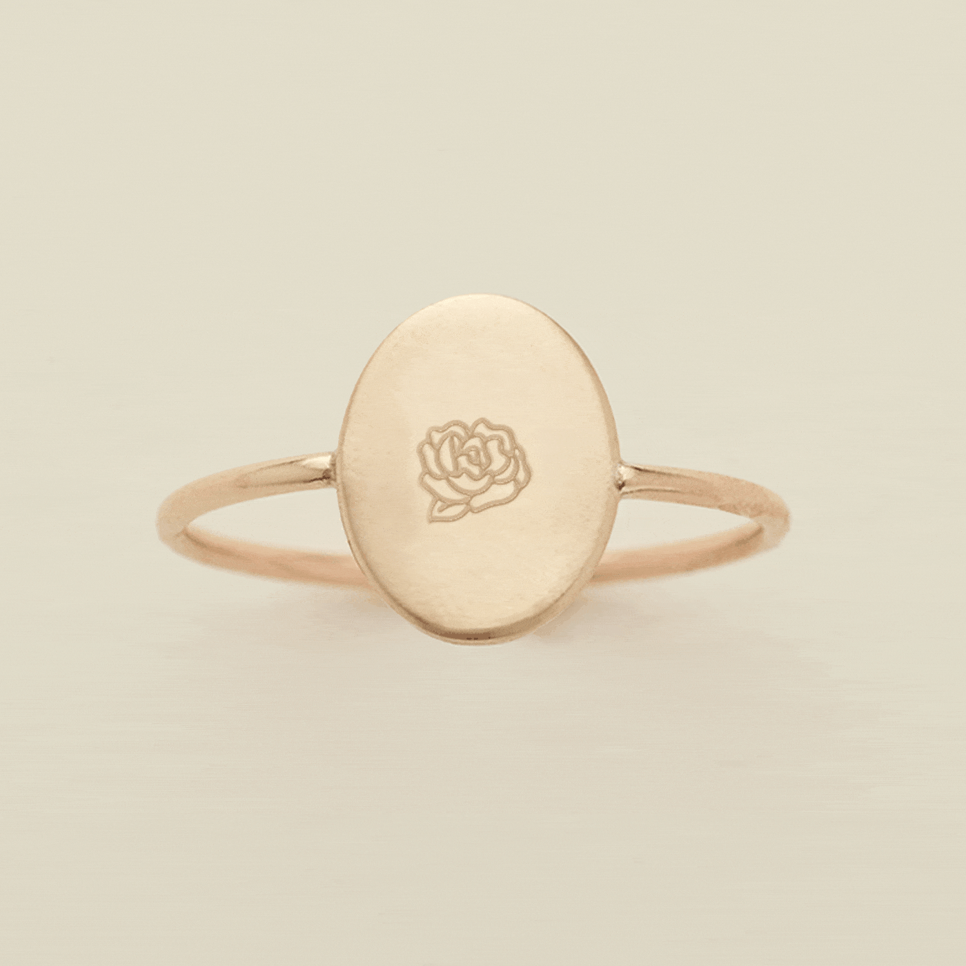 A gif of a dainty gold wire ring with a flat oval in the center, with different engraved designs cycling through one by one. There are initials and various floral motifs.