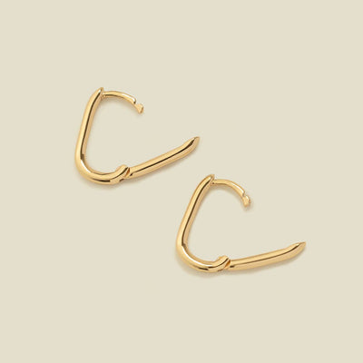 A pair of rounded rectangle hoop earrings laying flat on a solid light beige surface, each with the latch open to show the hinge closure.