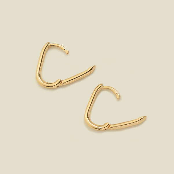 A pair of rounded rectangle hoop earrings laying flat on a solid light beige surface, each with the latch open to show the hinge closure.